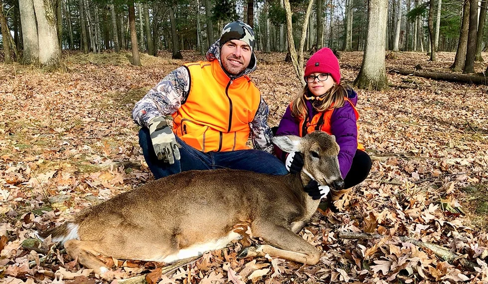 Couple posing with deer during hunting expedition in forest