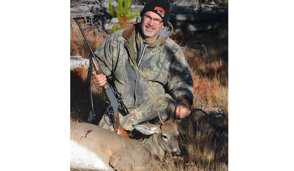 Deer hunter with Henry lever-action rifle in outdoor wilderness setting