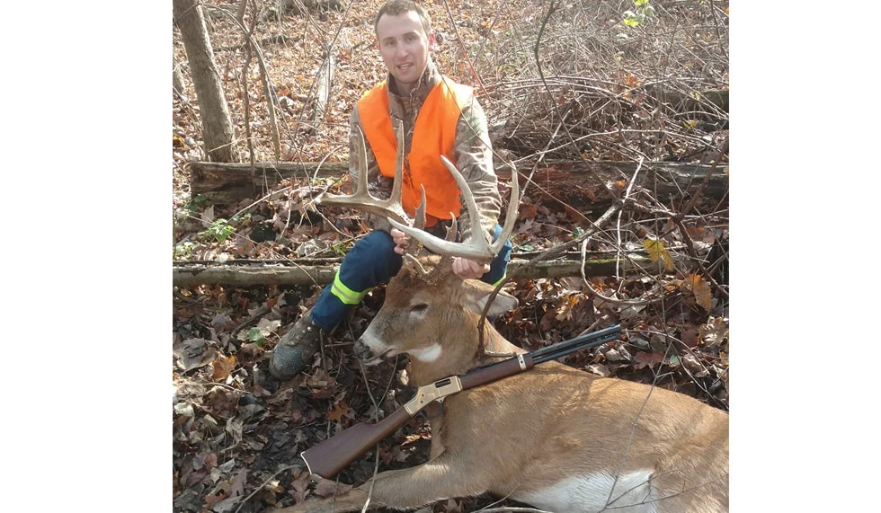 Hunter posing with harvested deer while using Henry Repeating Arms firearm in outdoor setting