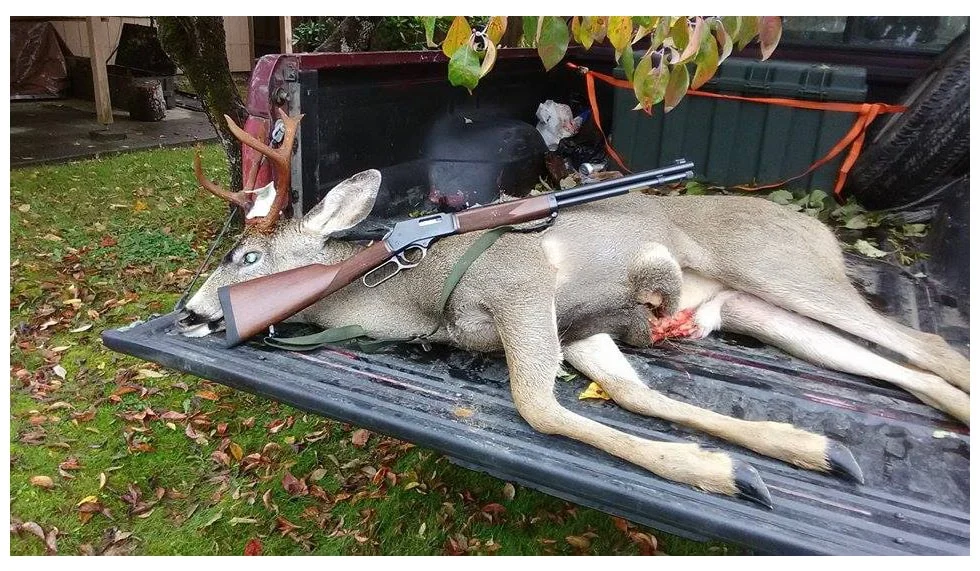 Henry lever-action rifle next to deceased deer for large game hunting