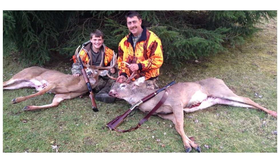 Two hunters pose with a large deer they hunted using a Henry lever-action rifle, a popular choice for big game pursuits in North America