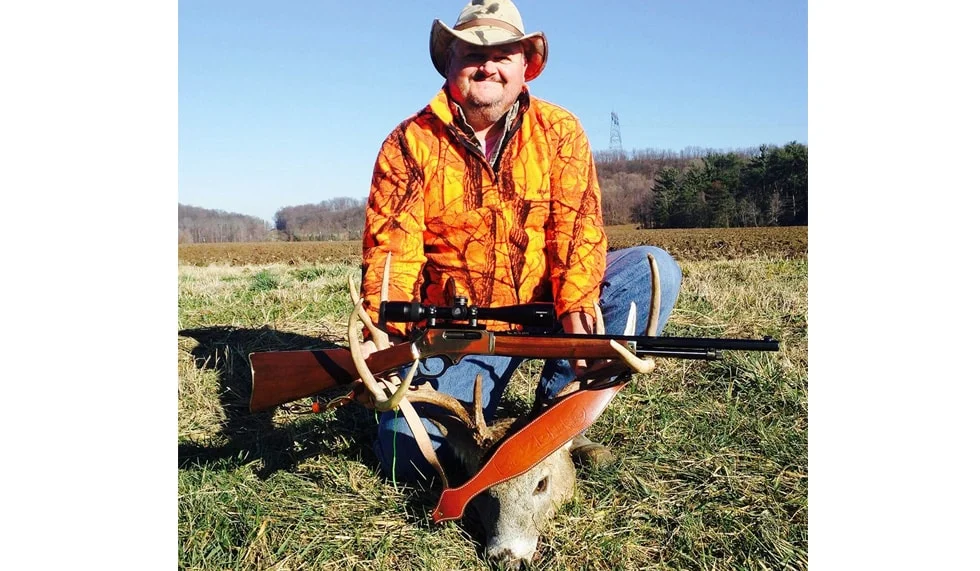 Hunter in orange jacket holding Henry lever-action rifle in field