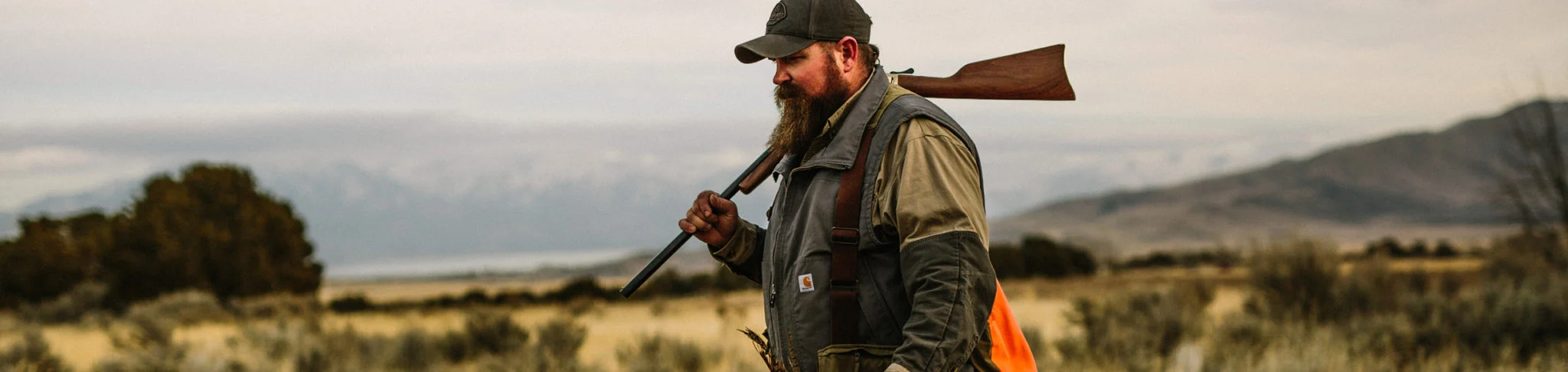 Hunter with bolt-action rifle surveying rural landscape