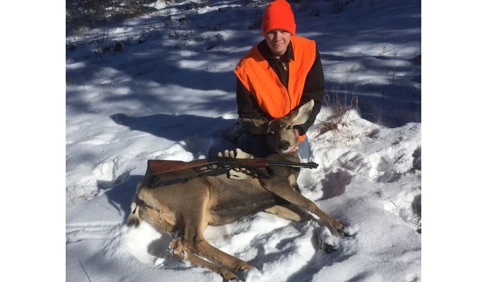 Hunter in orange jacket posing with deer he shot using a Henry rifle in a snowy outdoor setting