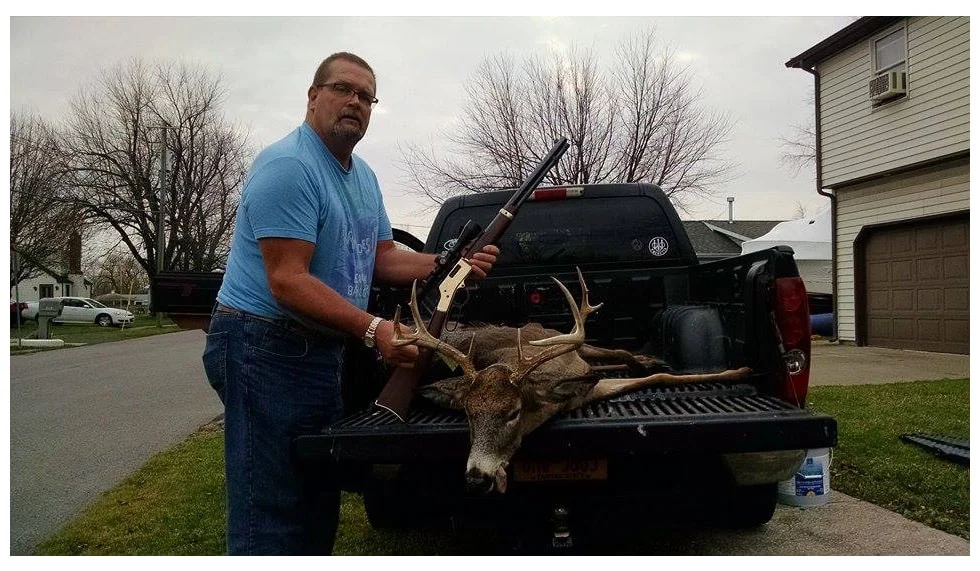Hunter proudly displays trophy deer in back of pickup truck, Henry Repeating Arms rifle and company name visible