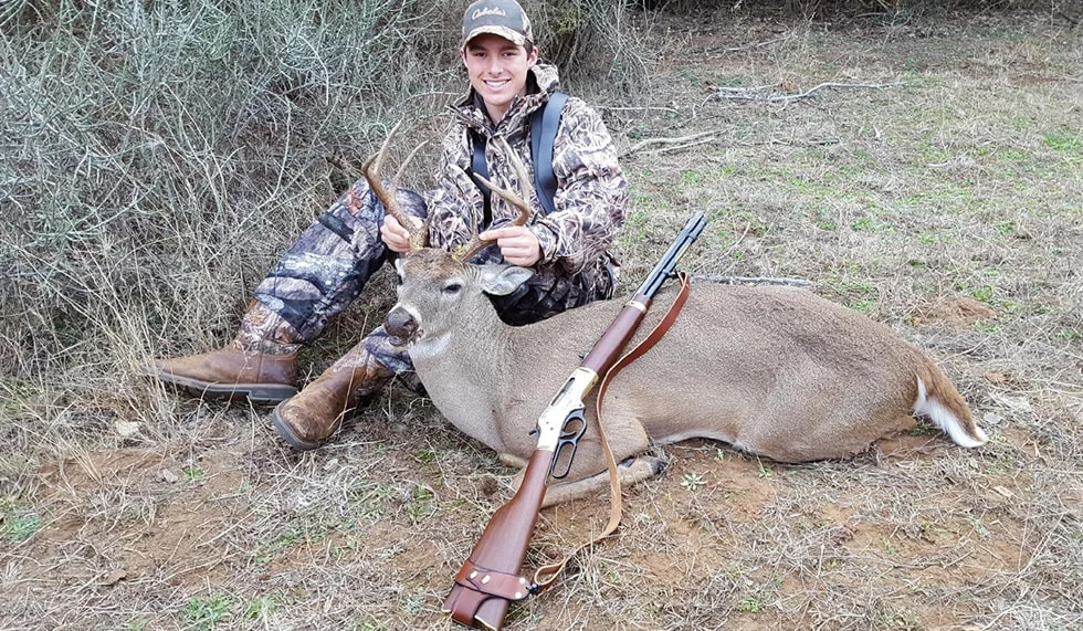 Hunter posing with trophy deer kill, holding Henry lever-action hunting rifle