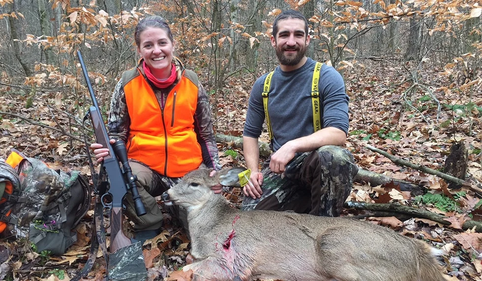 Two hunters posing with a deer they have hunted in a forested outdoor setting