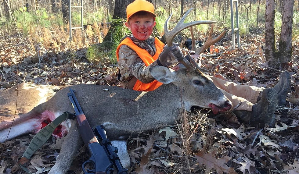 Large whitetail deer trophy taken by a hunter wearing Henry Repeating Arms hunting gear in a wooded forest setting