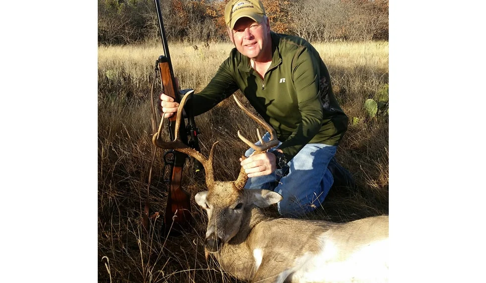 Man holding deer trophy in wooded outdoor setting, Henry Repeating Arms rifle visible