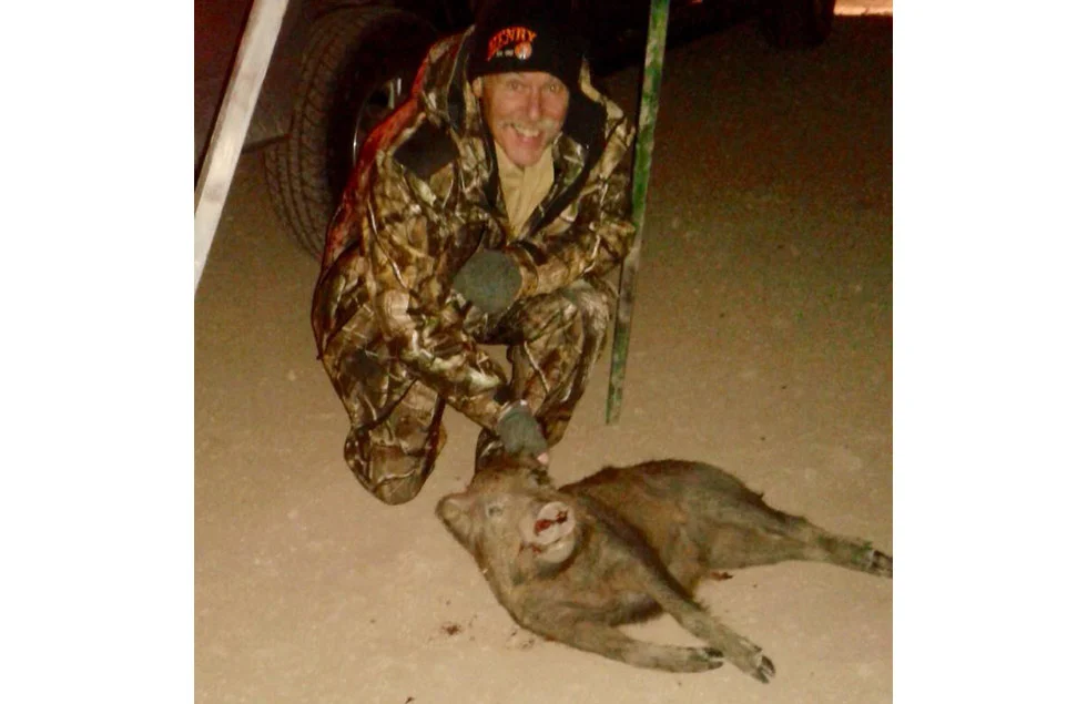 Night hog hunting in camouflage gear, with a large feral hog on the ground
