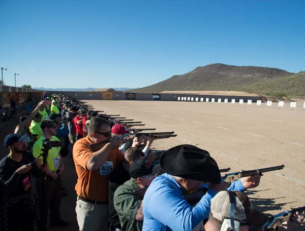 A line of shooters aiming down the sights of their rifles in the desert at the Henry 1,000 Man Shoot.