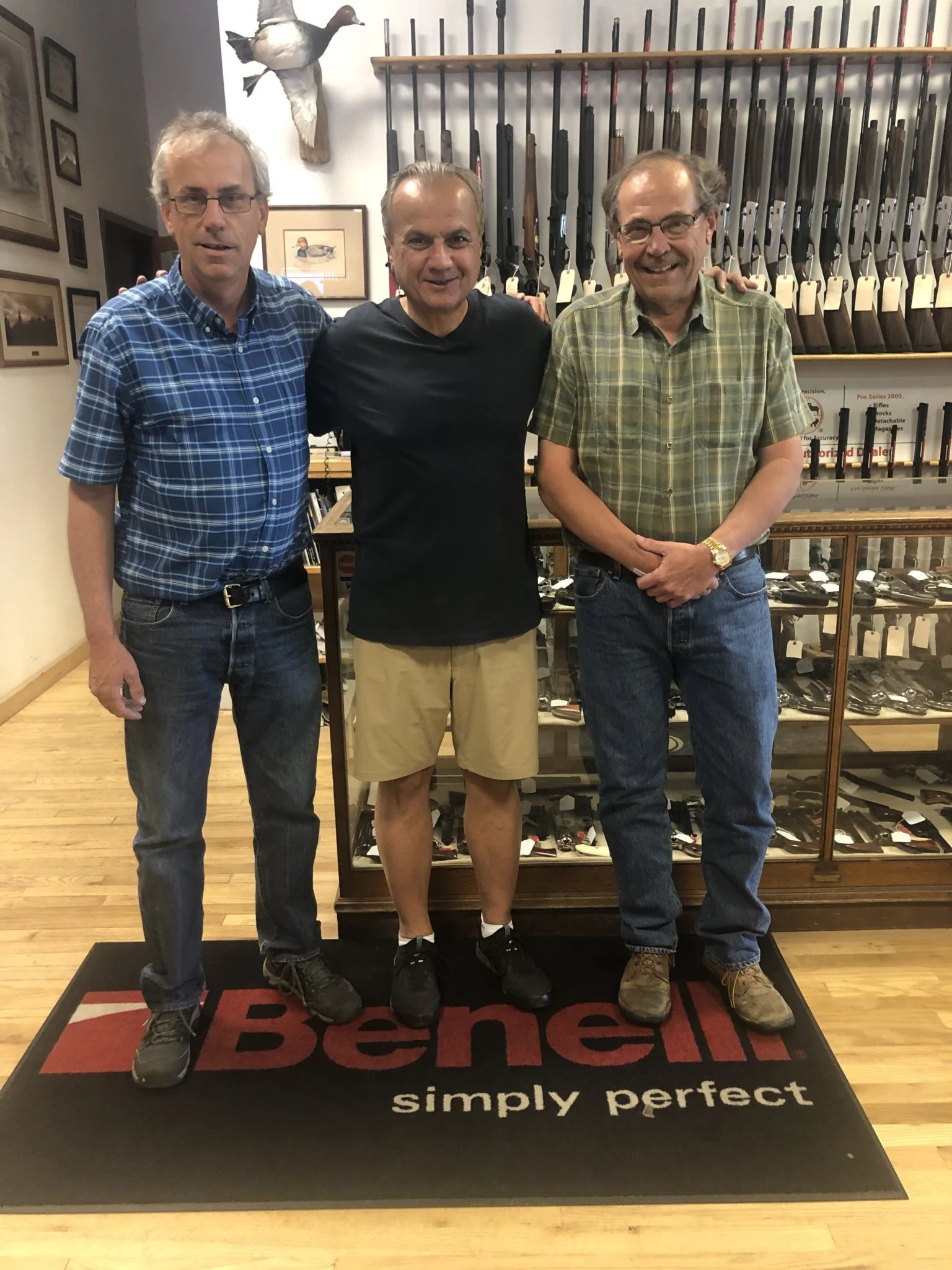 Three men standing in gun shop with Henry Repeating Arms branding, showcasing firearms selection