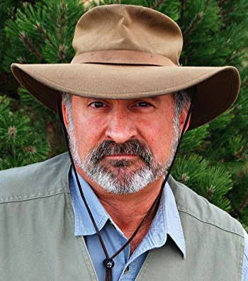 Rugged outdoorsman wearing wide-brimmed hat, beard, and casual clothing