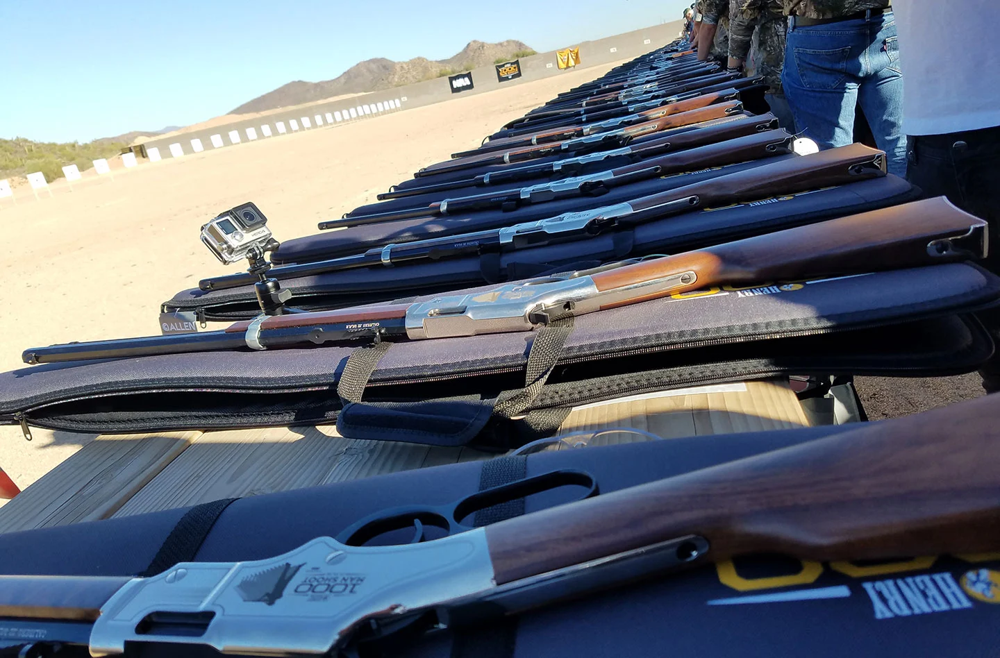 Assortment of lever-action rifles, revolvers, and other firearms displayed on a table in an outdoor setting