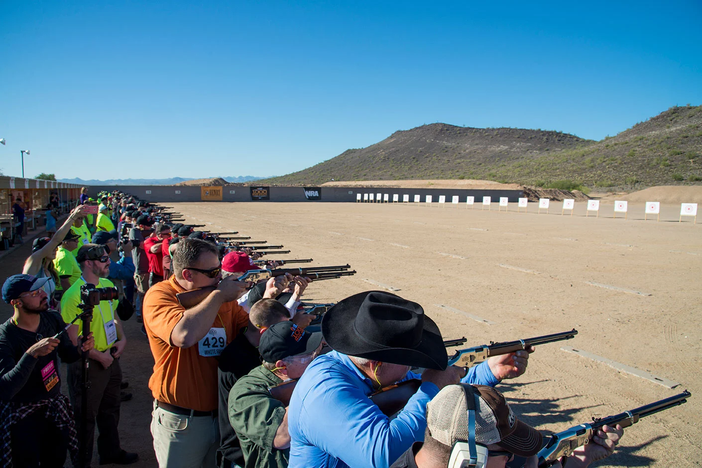 Large group of people firing rifles at an outdoor shooting range to celebrate the 1,000 Man Shoot anniversary event hosted by Henry Repeating Arms