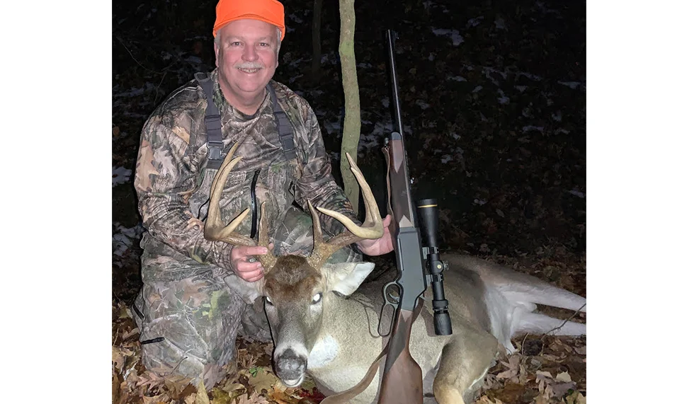 Hunter in camouflage clothing posing with a harvested white-tailed deer