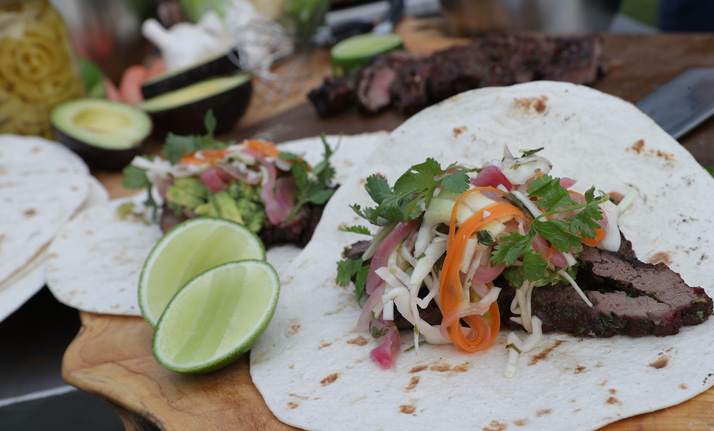 Spicy bear meat tacos on a wooden table with lime wedges and fresh herbs