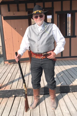 Senior man in cowboy-style outfit holding rifle on wooden deck