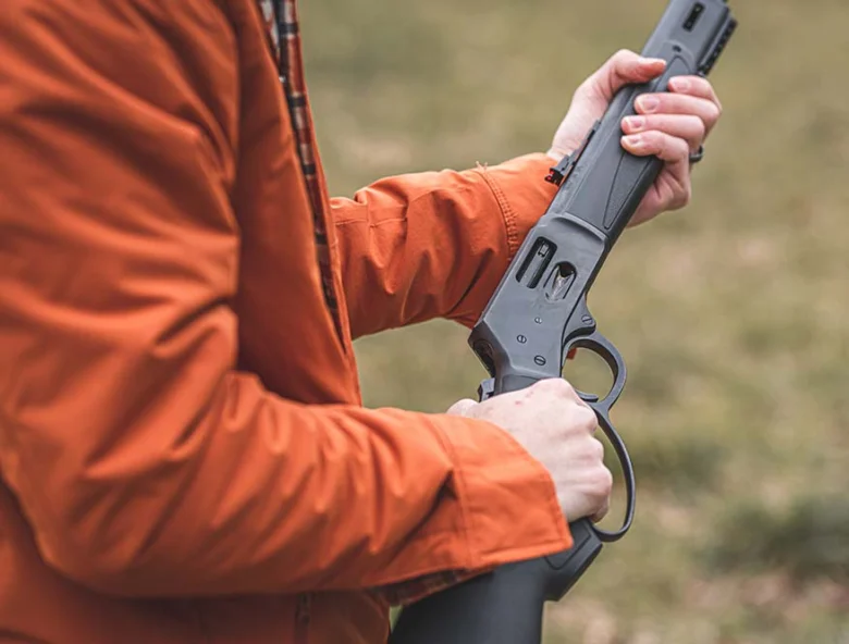 Person in orange jacket holding a lever-action rifle in an outdoor setting