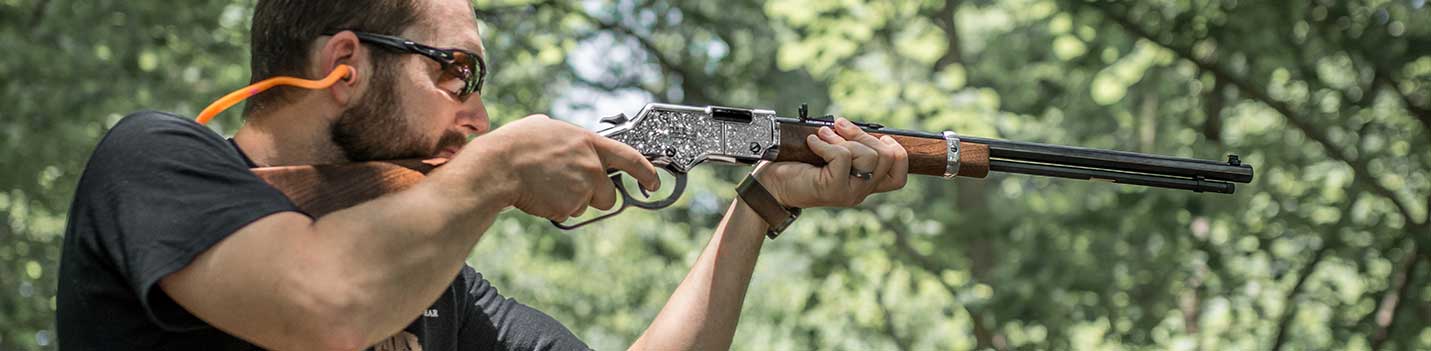 Person aiming and shooting a Henry lever-action rifle in the forest