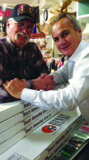 Two men shaking hands in front of Henry lever-action rifles on display