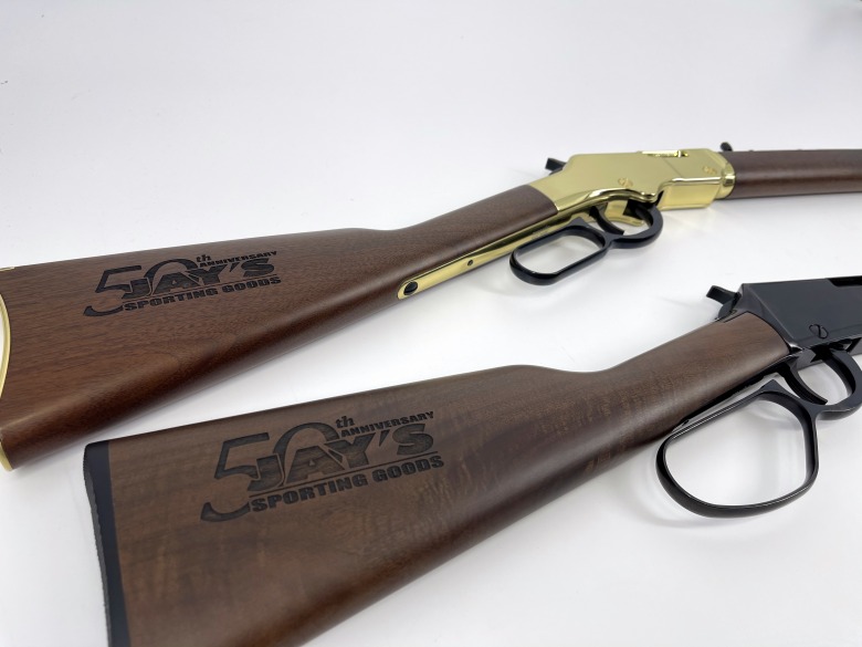 Wood buttstocks on two different rifles showing engraved 50th anniversary logos
