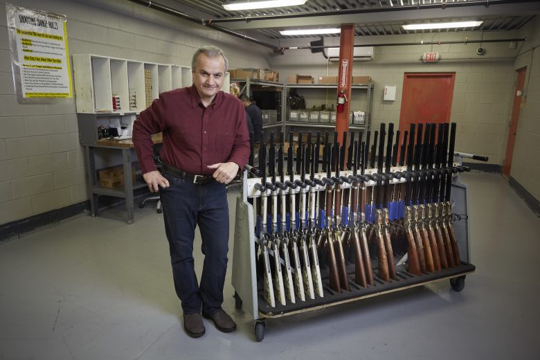 Anthony Imperato leaning against a rack of rifles in a factory setting
