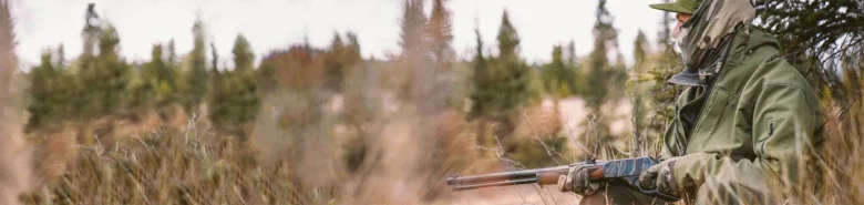 Hunter crouched in nature wielding a reliable, American-made Henry rifle for a successful hunt