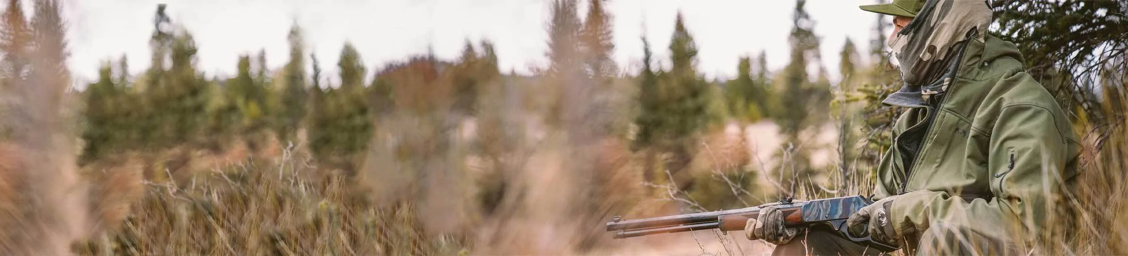 Hunter in camouflage gear carrying a Henry lever-action rifle in a forested outdoor setting