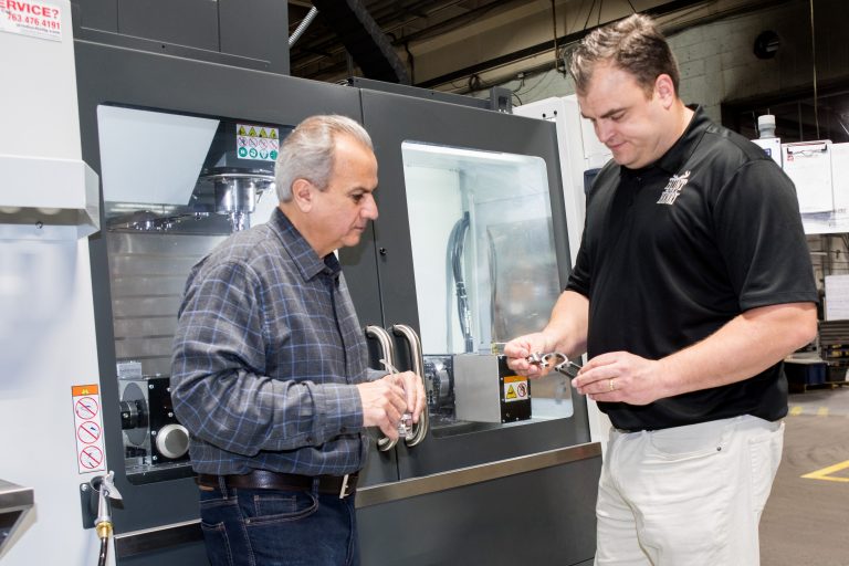 Anthony Imperato and Andy Wickstrom reviewing a lever next to a Haas CNC machine.