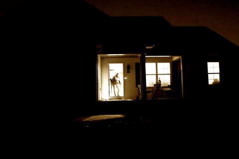 View of a house at night with a woman standing in the doorway with a rifle