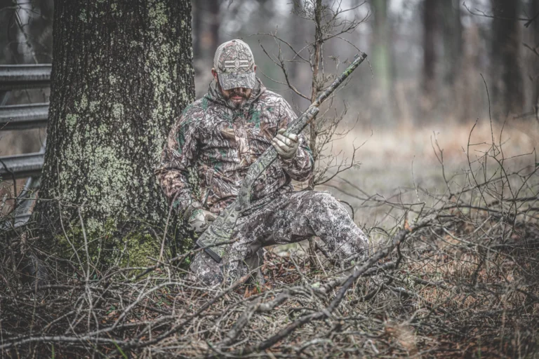 Camouflaged hunter crouching in forest with tactical shotgun