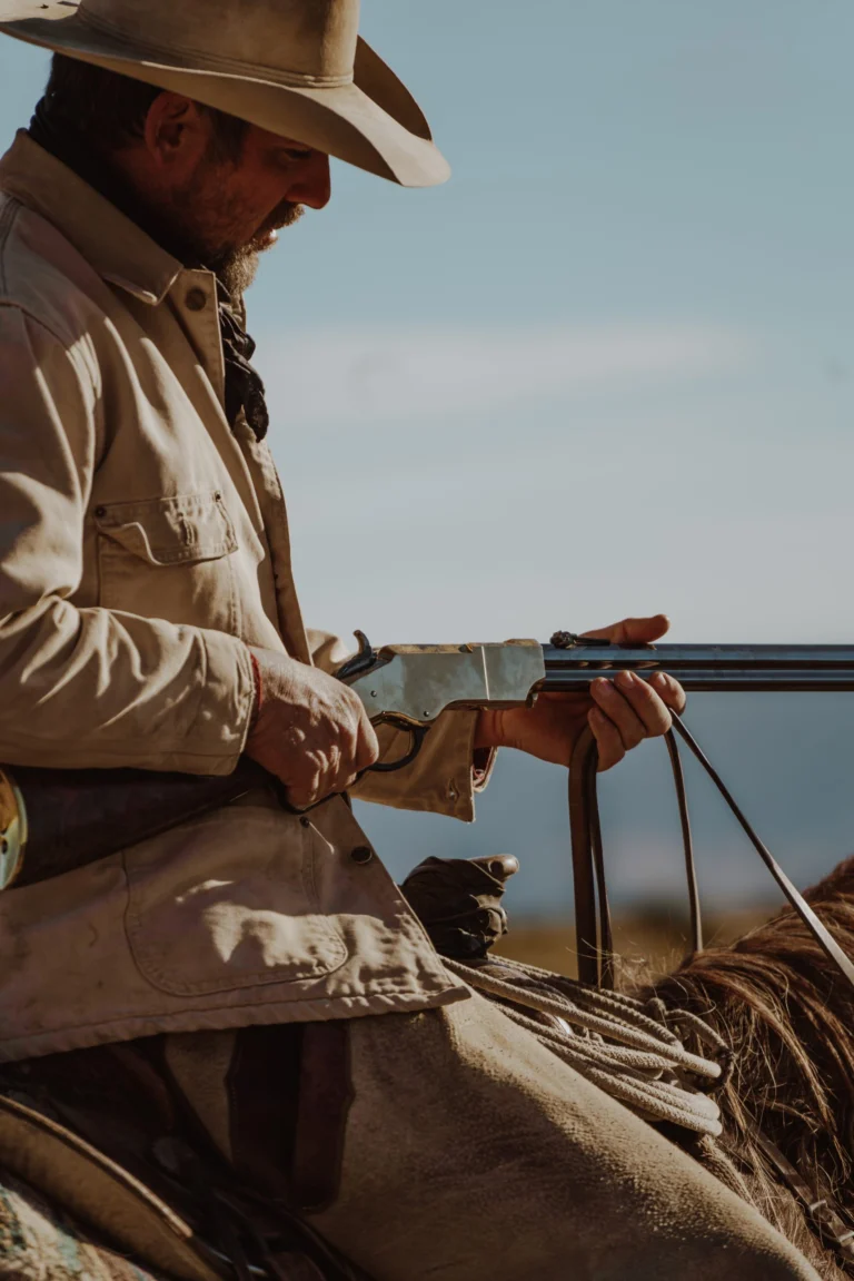 Cowboy wearing wide-brimmed hat holding a Henry lever-action rifle in a Western landscape