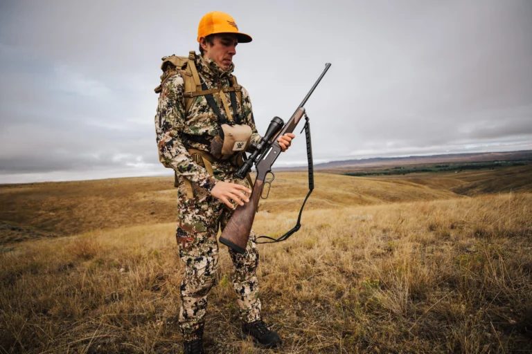 Hunter in tactical gear carrying a Henry rifle in a grassy field