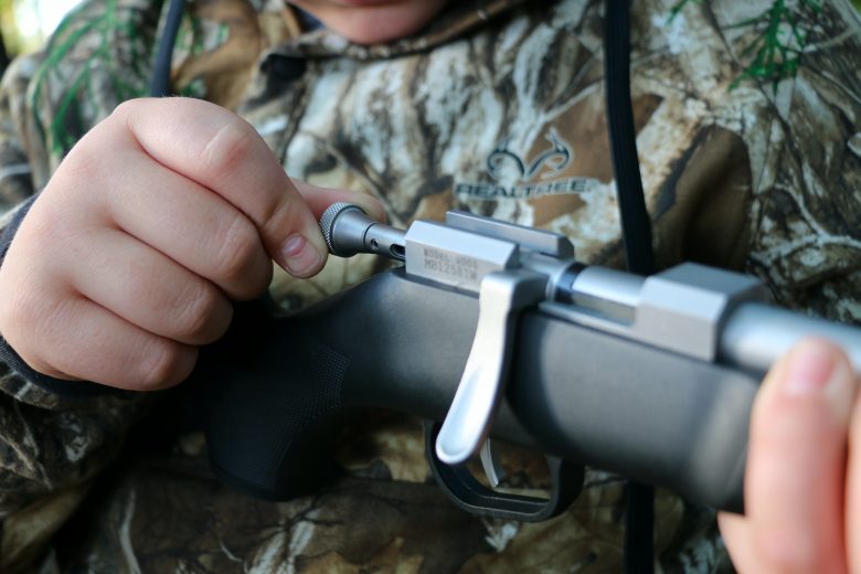 A youth hunter pulling back the safety switch on a bolt action rifle