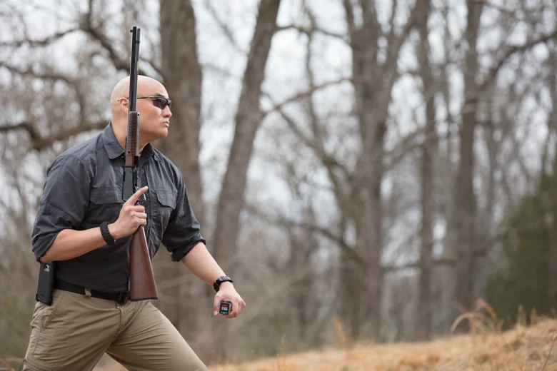 Man holding rifle and ammunition box in forested outdoor setting