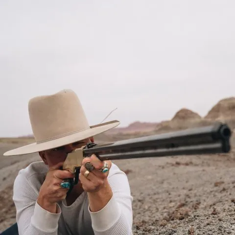 Man with a Stetson hat aiming a Henry rifle