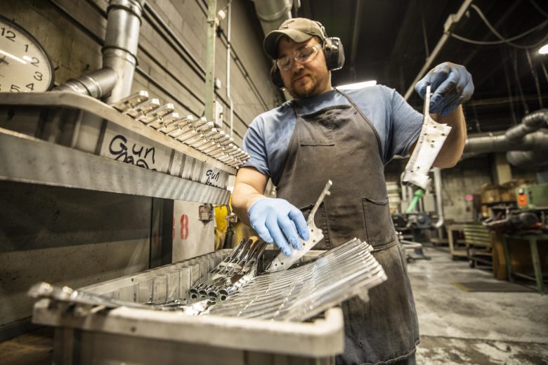 Man in a factory putting parts into a plastic bin.