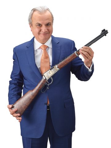 Anthony Imperato in a suit smiling while holding an engraved rifle.