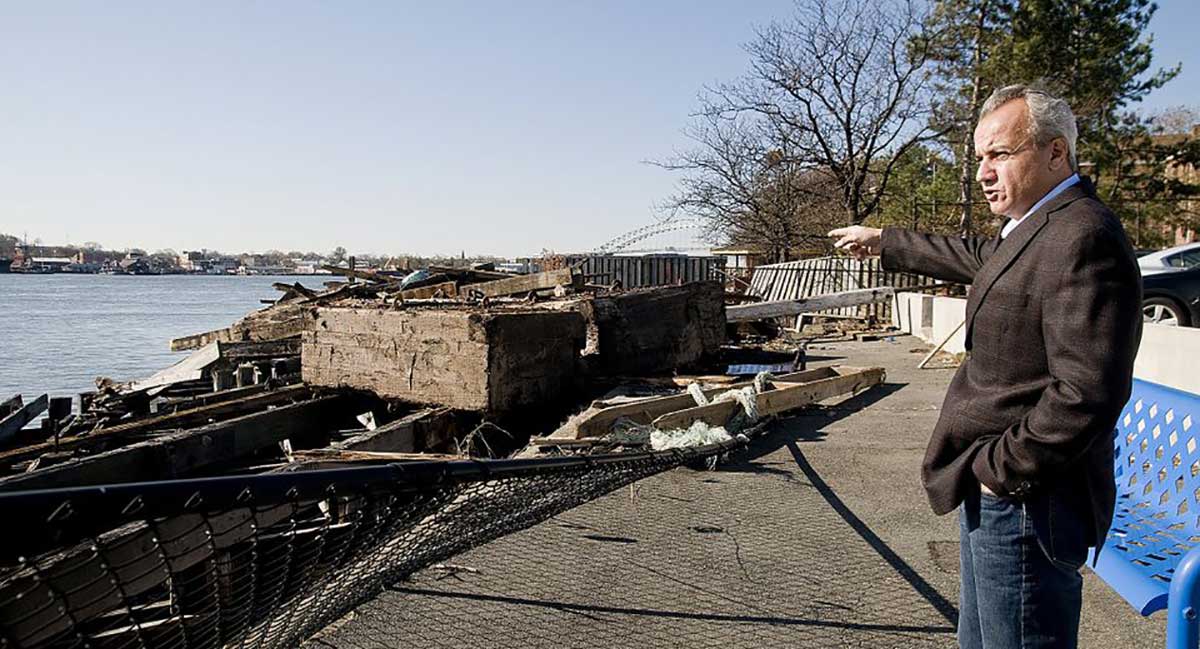 Waterfront scene with old wooden fishing boats and a man in a suit standing on the pier, celebrating 25 years of Henry Repeating Arms