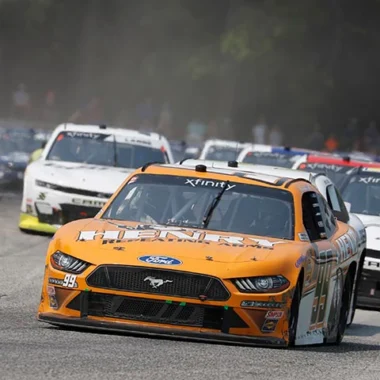 NASCAR racing car, an orange Ford Mustang, competing on the racetrack at night