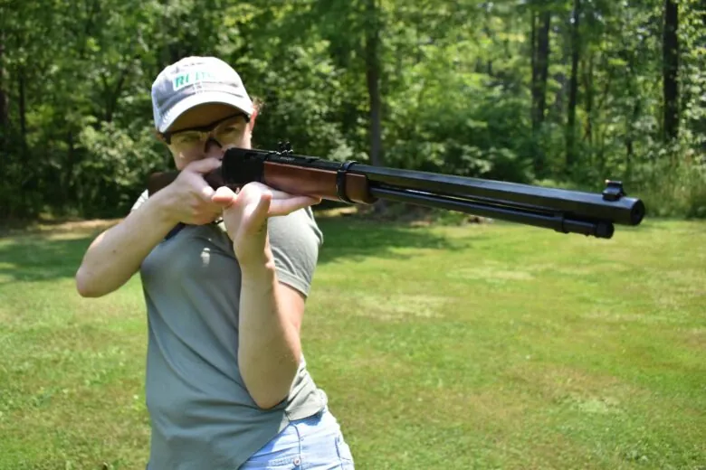 Woman holding up a rifle in an offhand shooting position.