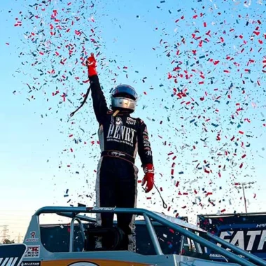 Race car driver raising arms in celebration as confetti falls around them after winning a race