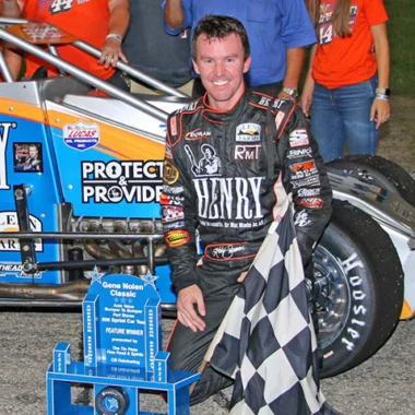 Race car driver posing next to a race car bearing the Henry Repeating Arms logo