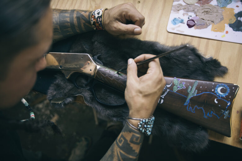 A person painting a rifle that's laying down on a bearskin hide on a table.