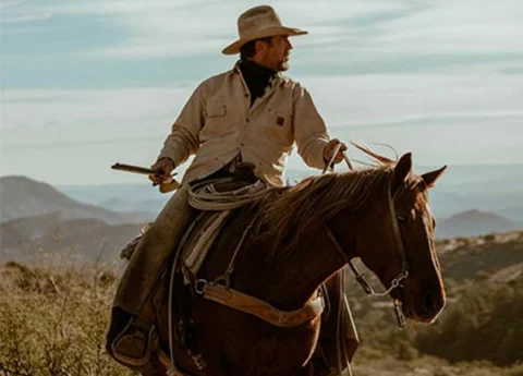 Cowboy riding horse through rural landscape
