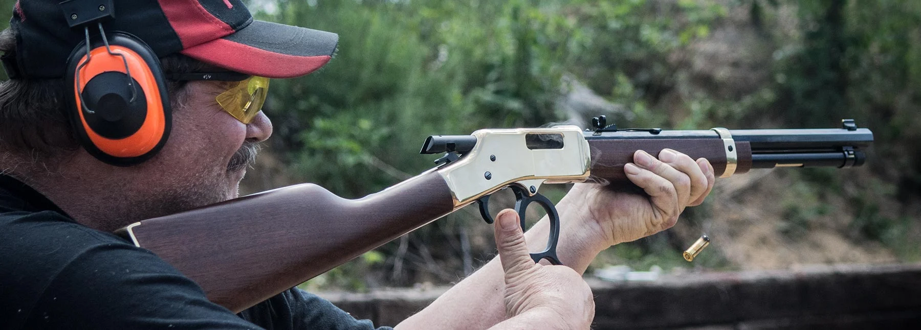 Person practicing firearm safety with protective gear in outdoor setting