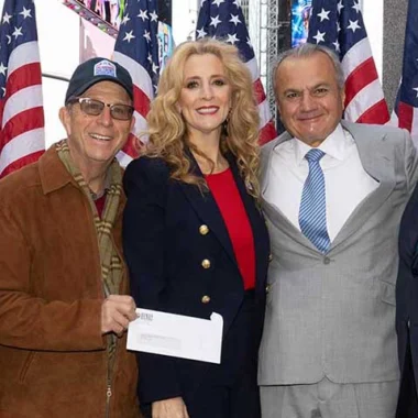 Three people smiling and posing in front of American flags