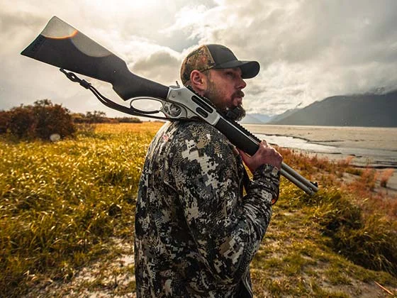 Outdoor hunter holding lever-action rifle in field with mountains in background