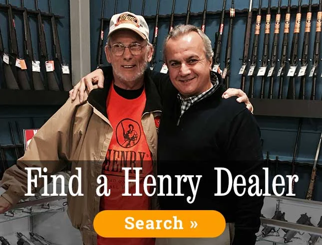 Two men smiling and embracing in front of firearm display, promoting Henry Repeating Arms dealer partnership